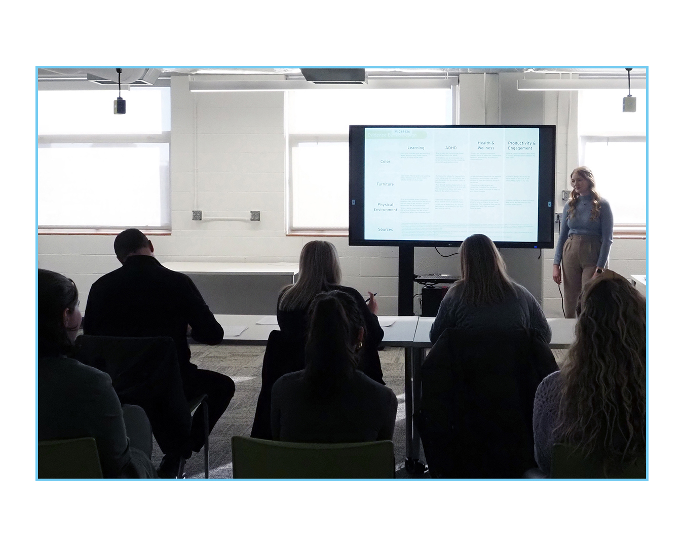 Student presents architectural plan on large digital display to seated audience in studio.