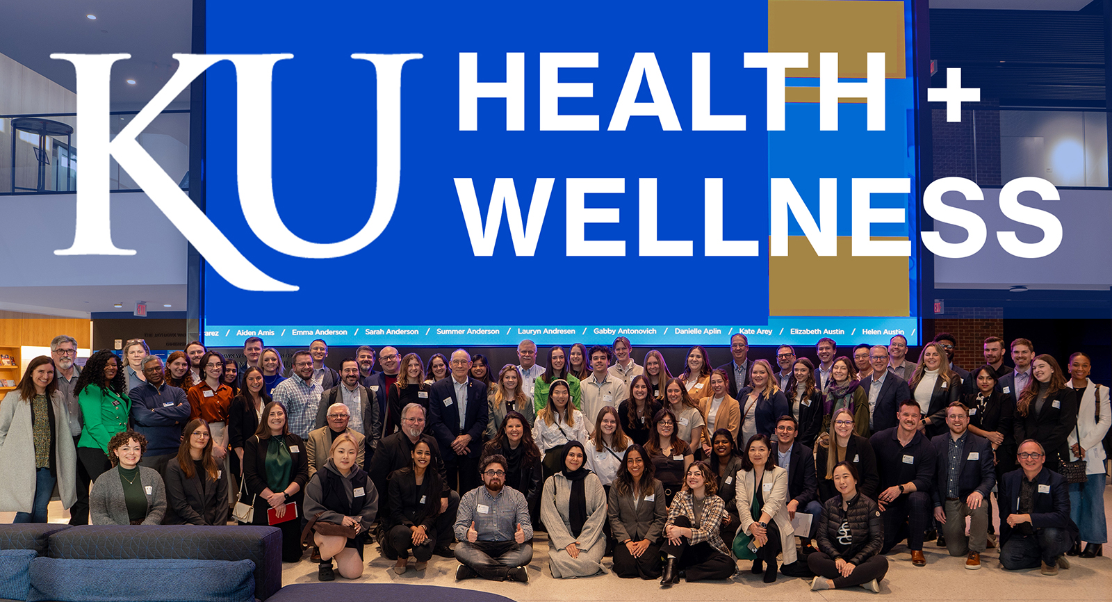 Text reads 'KU Health + Wellness" over color photograph of large group of people posed toward camera.