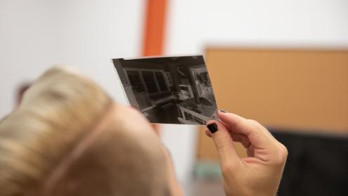 Color photograph shows student holding and looking through a 4"x5" large format film negative.