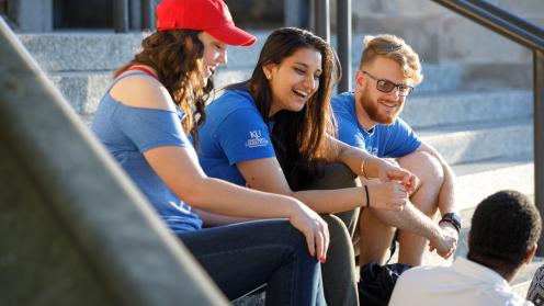 Color photograph of students smiling, talking on the steps of Watson Library.