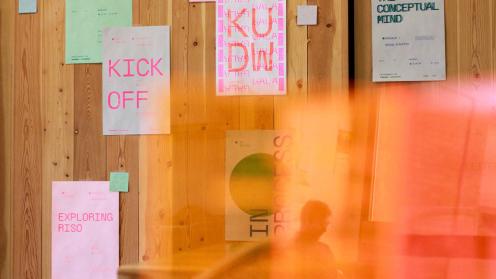 Color photograph shows Risograph-printed 2022 KU Design Week posters on wood wall in Chalmers Hall, University of Kansas.